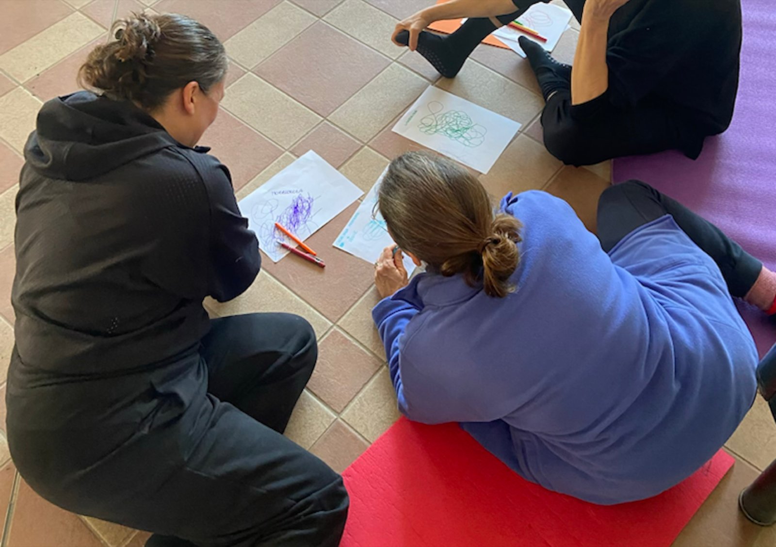 Due partecipanti sedute a terra di spalle durante un'attivita creativa
